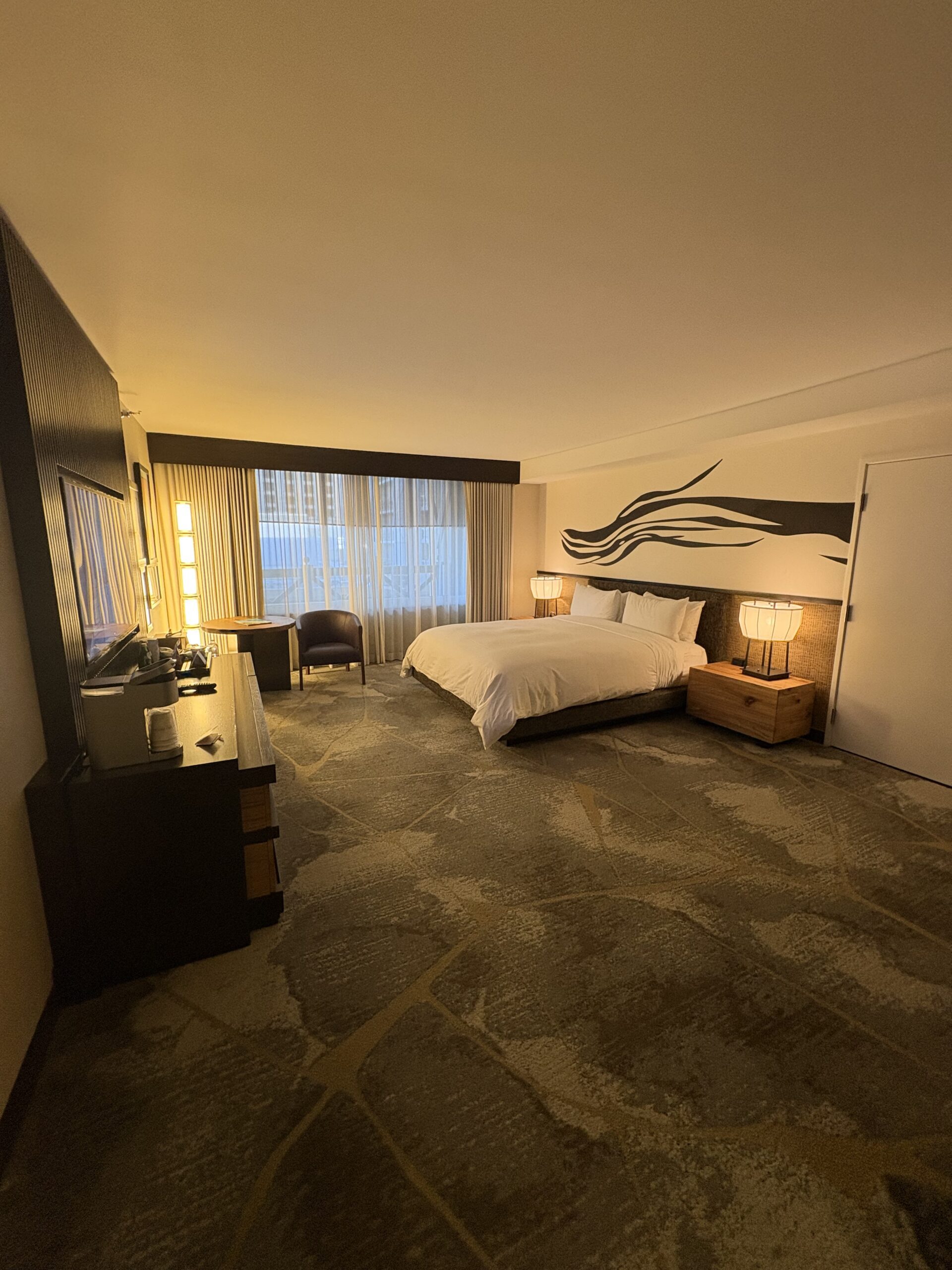 King bed with wood nightstand, table lamps, and abstract branch mural at Nobu Hotel Las Vegas