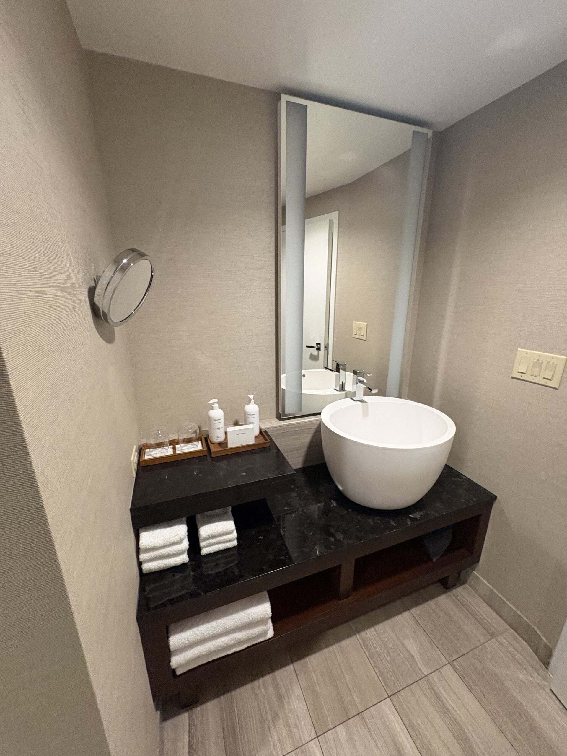 Modern bathroom vanity with round vessel sink, folded towels, and lit mirror at Nobu Hotel Las Vegas