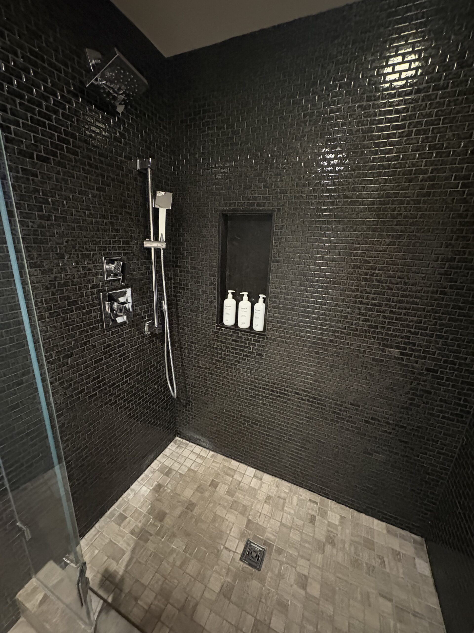 Black tile walk-in shower with rainfall showerhead and built-in product niche at Nobu Hotel Las Vegas