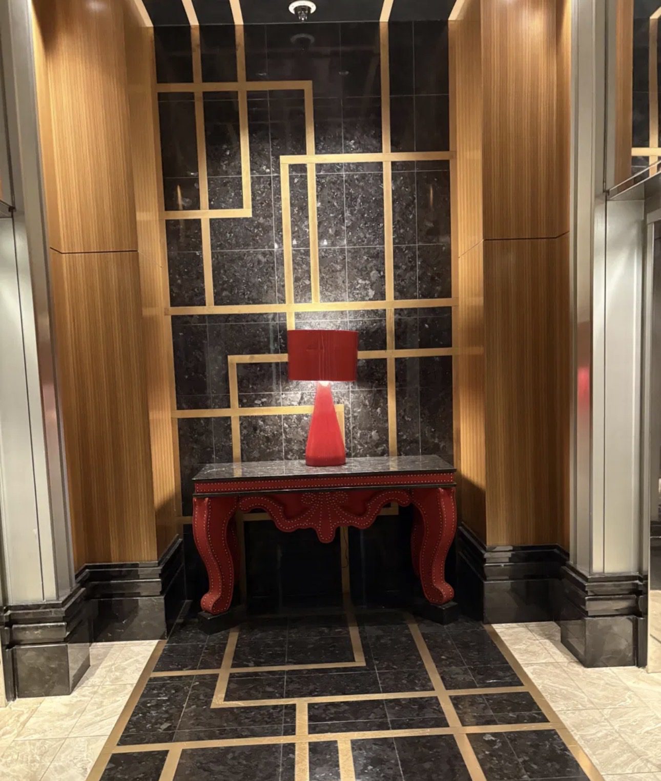 Red upholstered console table with matching lamp against a black and gold geometric wall at The Cosmopolitan Las Vegas