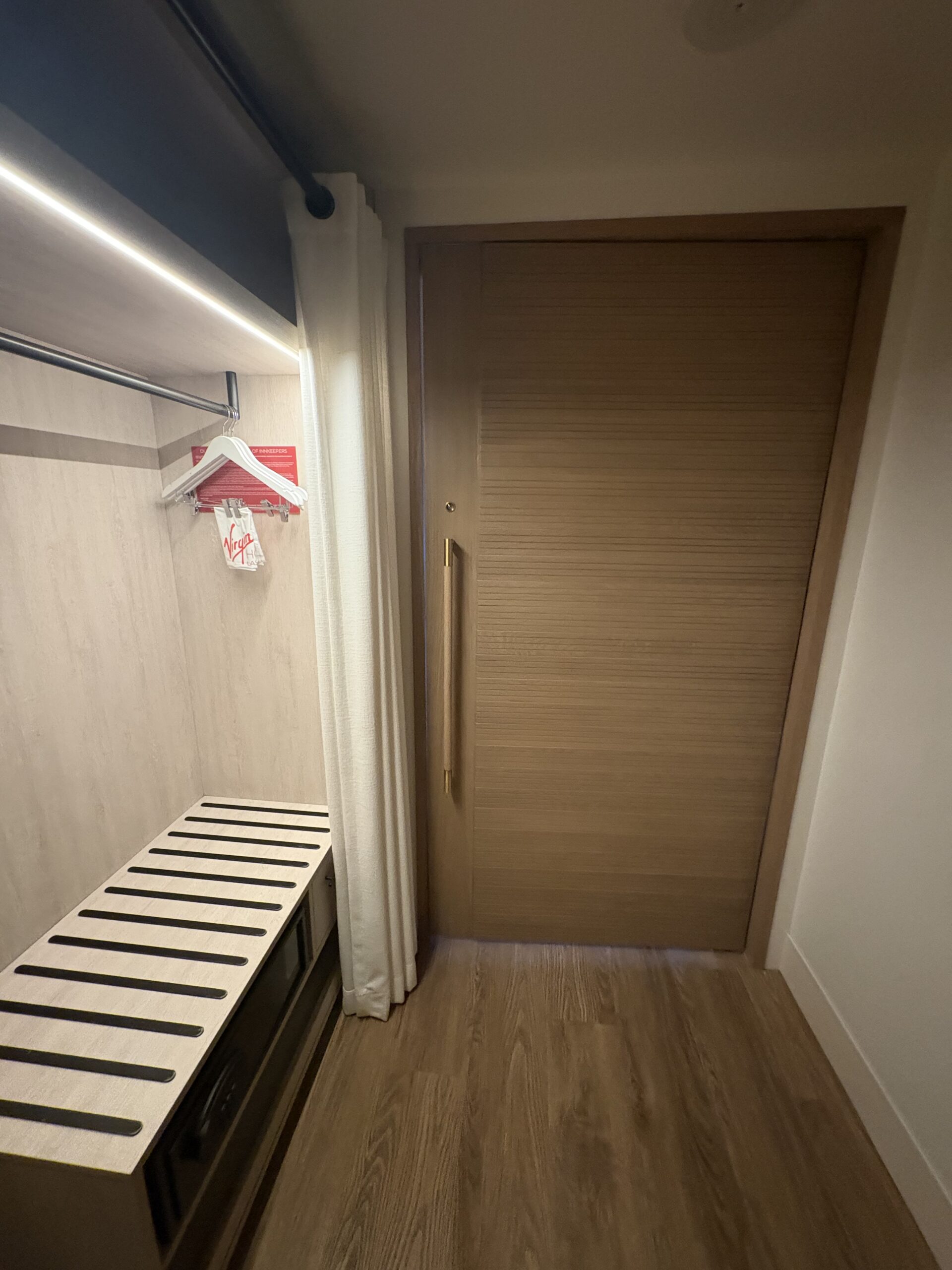 Open closet with luggage rack beside the slatted privacy door in a Virgin Hotels Chamber