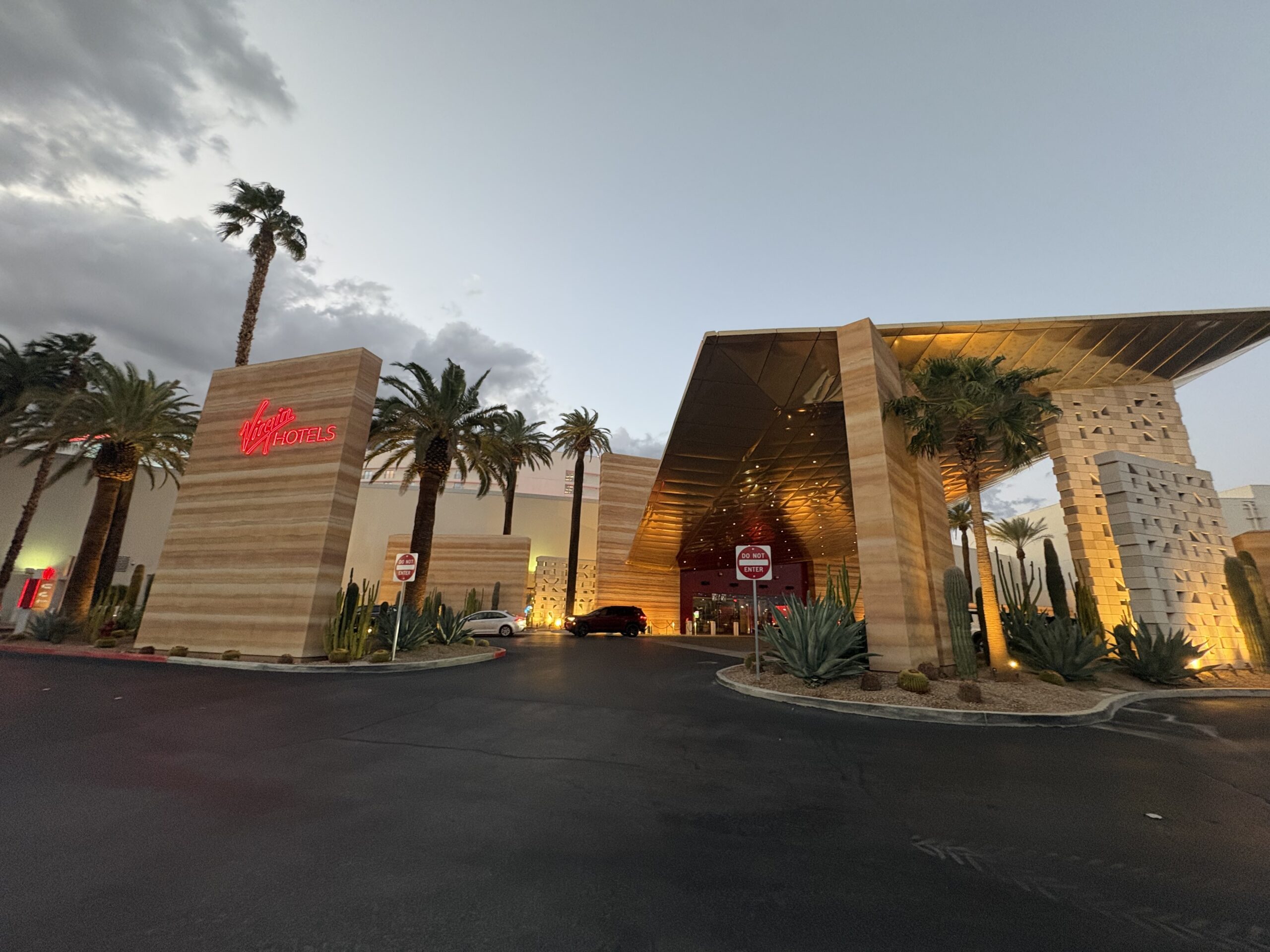 Virgin Hotels Las Vegas entrance with red neon sign, gold canopy, and cactus garden at dusk