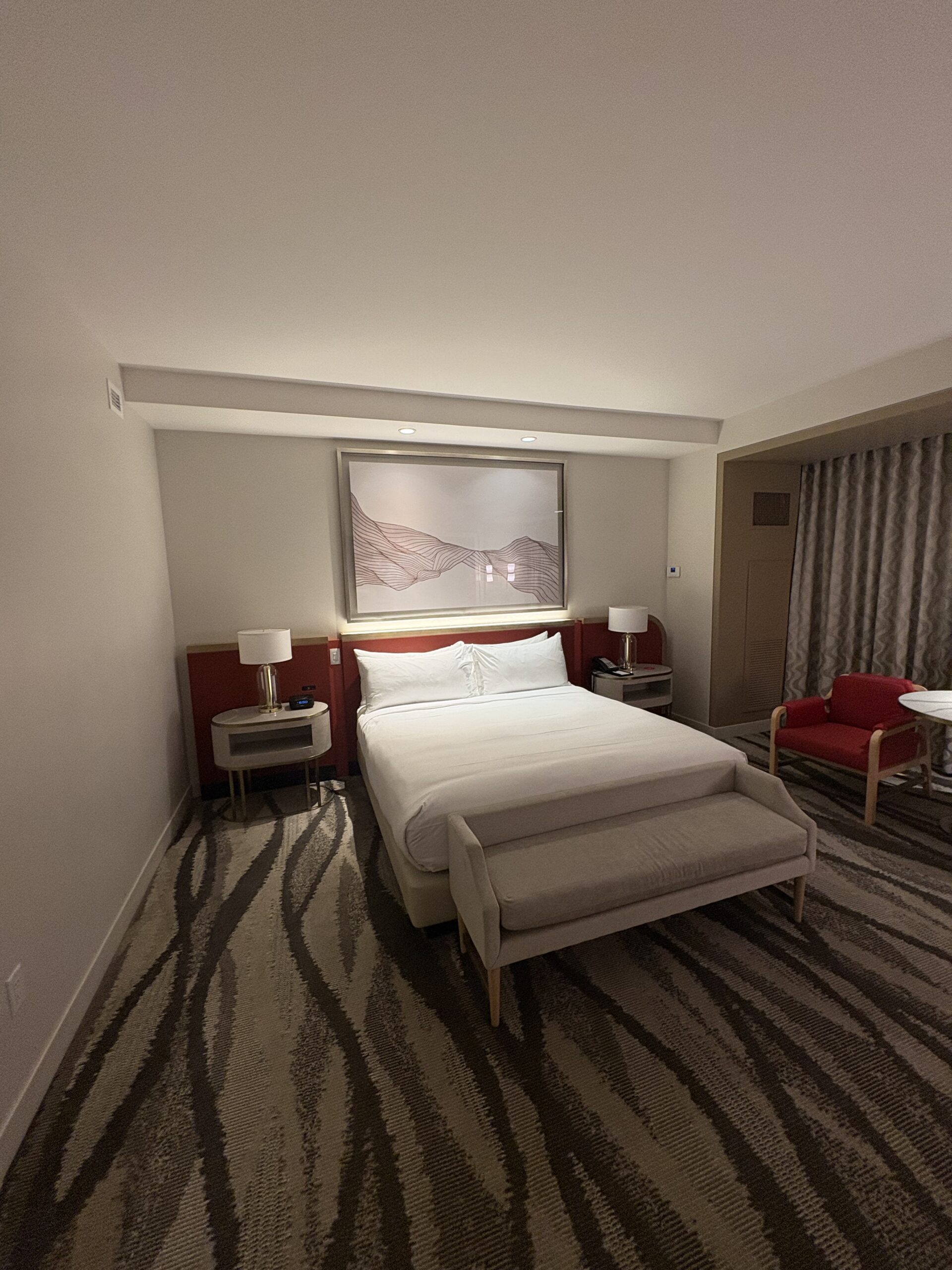 King bed with a red headboard and a bench at the foot of the bed in a Conrad Las Vegas room
