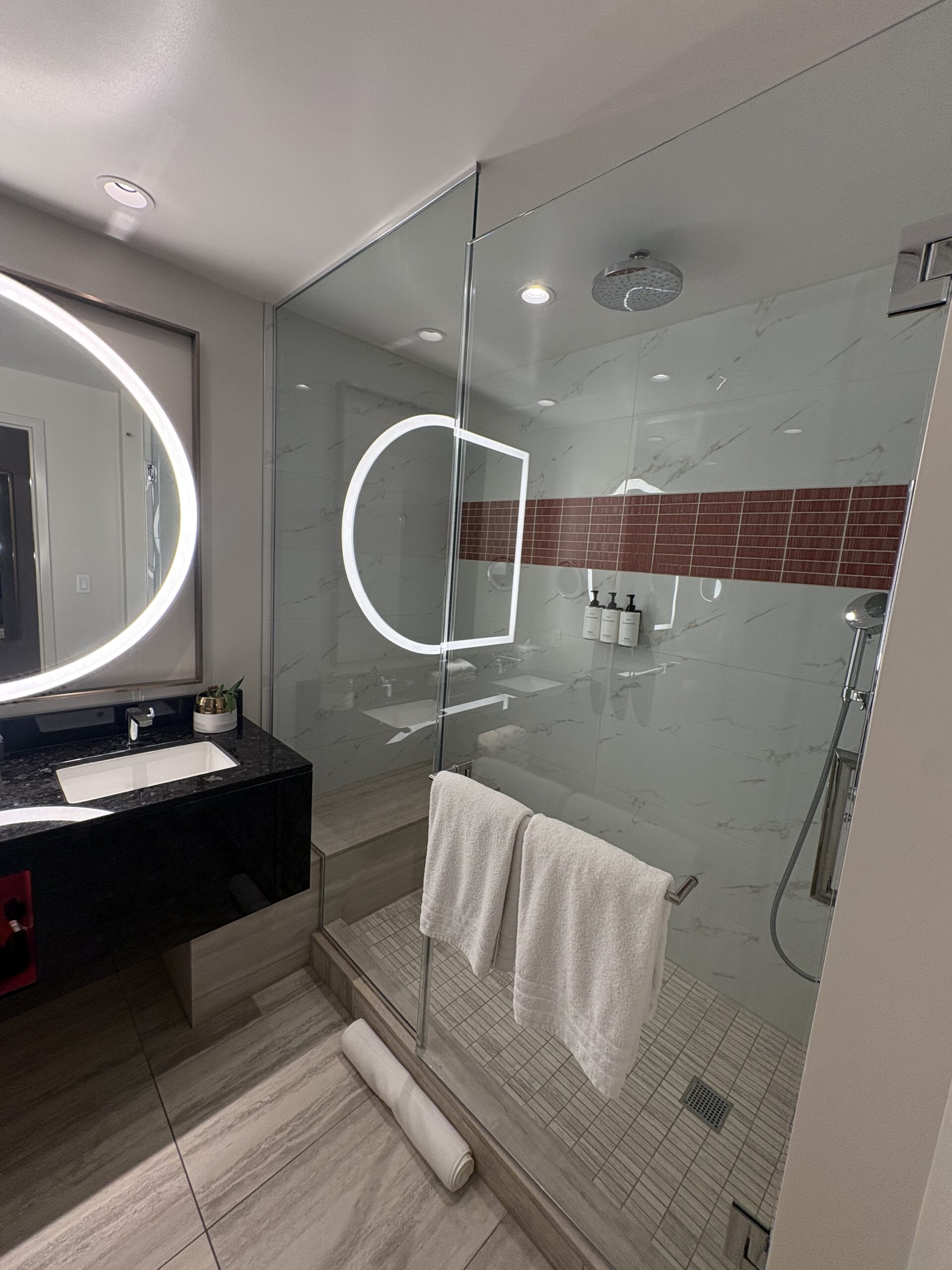 Glass-enclosed rain shower with a built-in bench and red accent tile in a Conrad Las Vegas bathroom