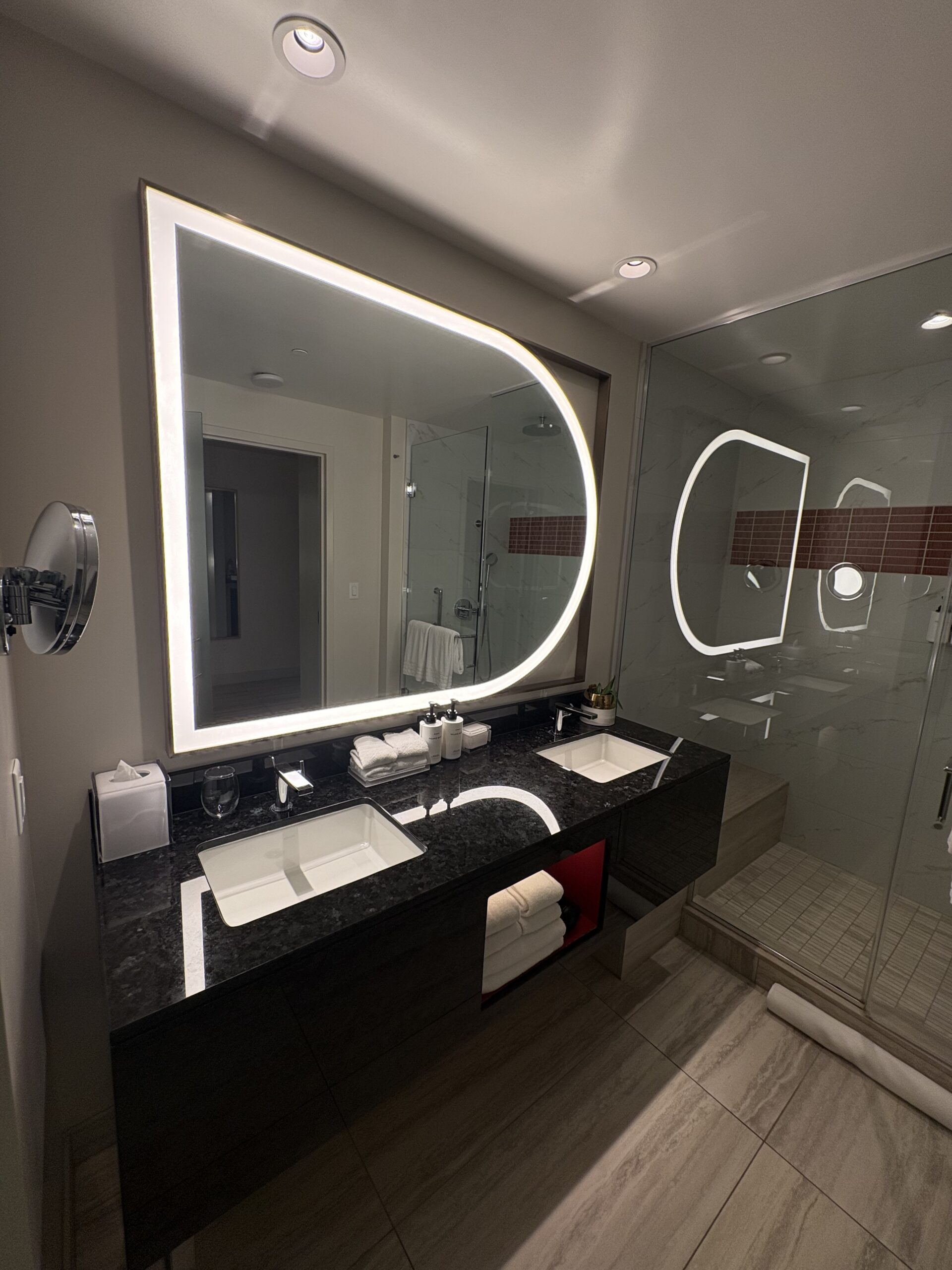 Double vanity with a black granite counter and large backlit mirror in a Conrad Las Vegas bathroom