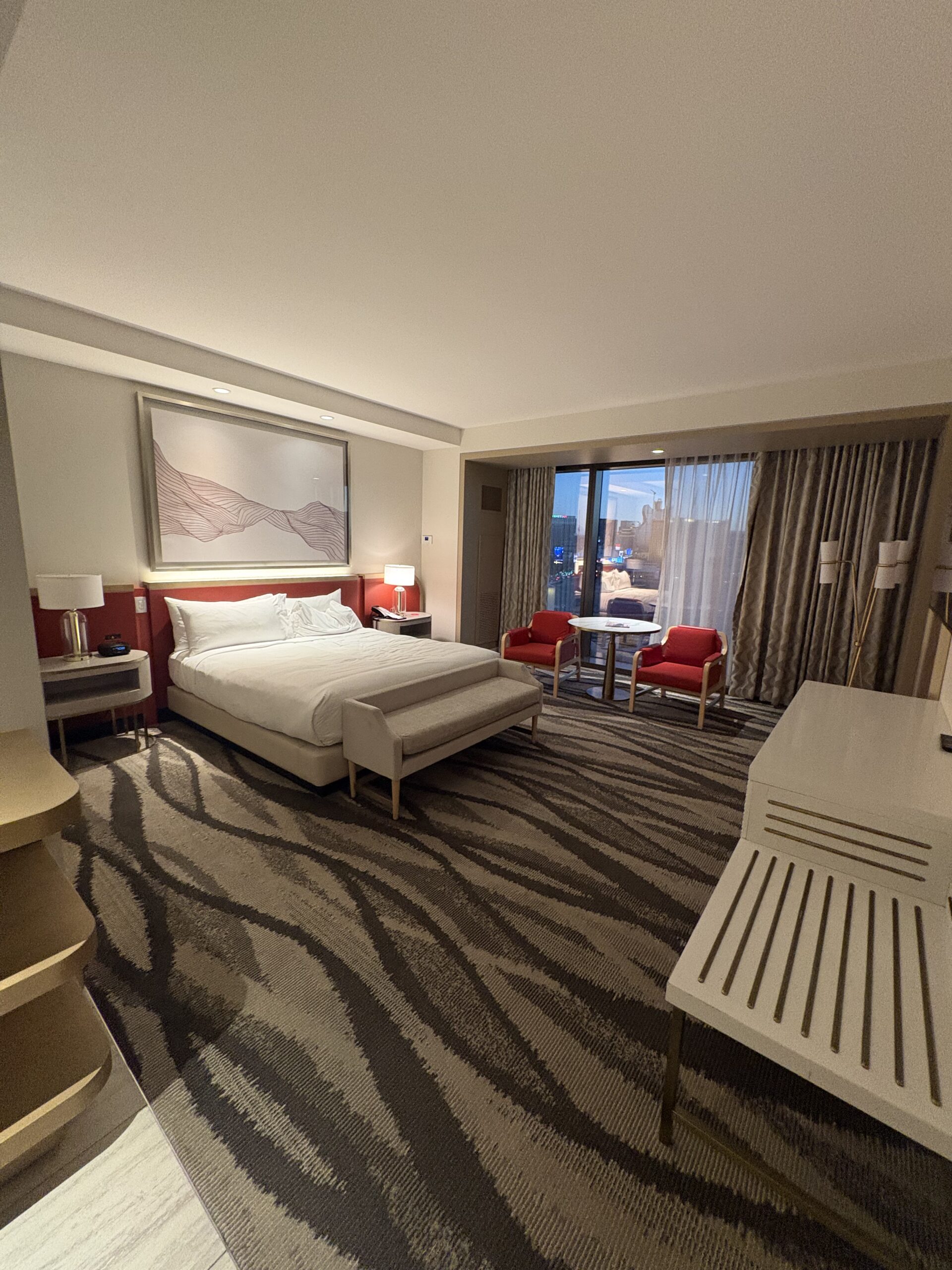 Conrad Las Vegas king room with bed, red accent chairs, and a window