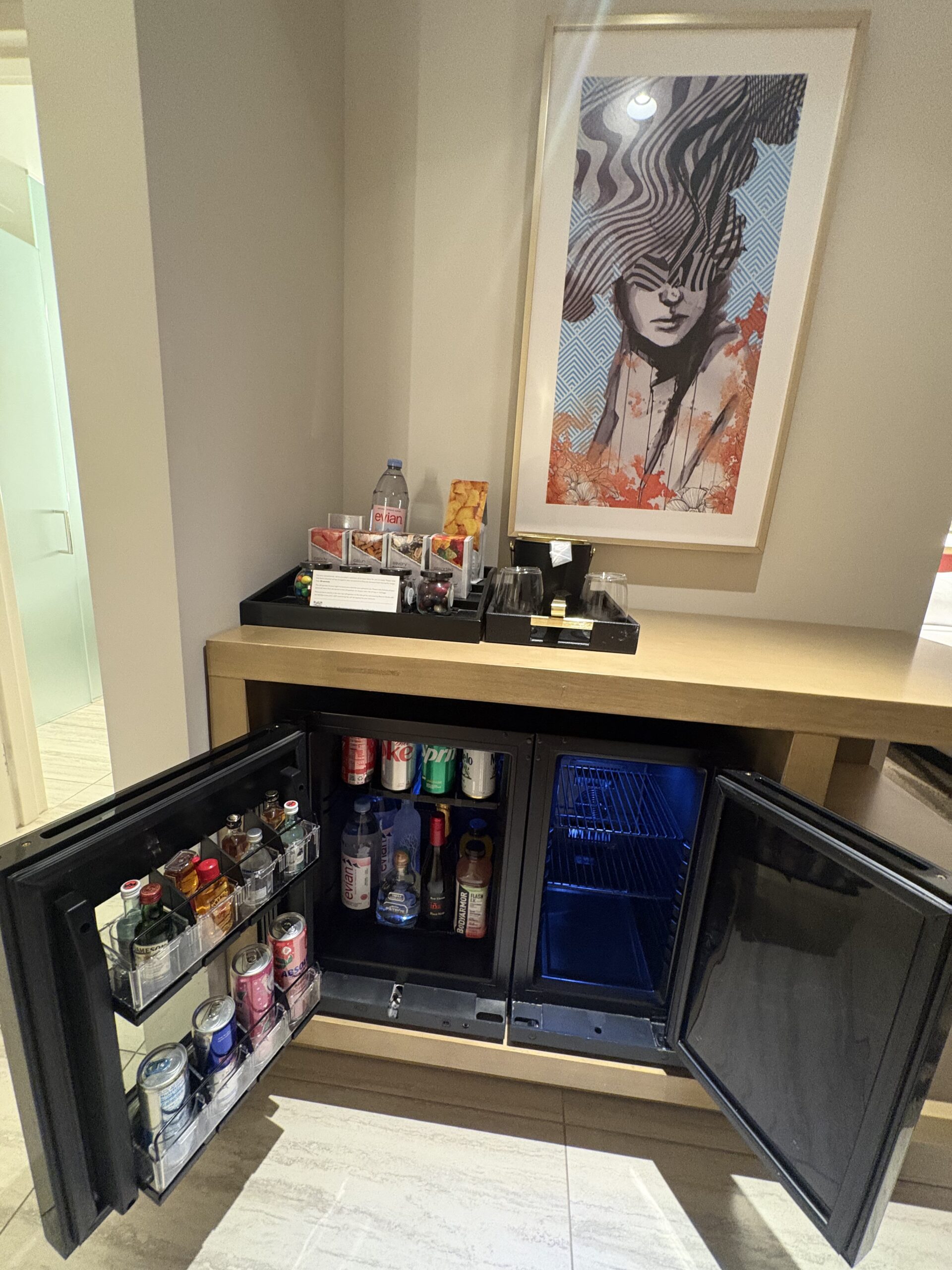 Two mini fridges side by side under framed art, one stocked minibar and one empty, in a Conrad Las Vegas room