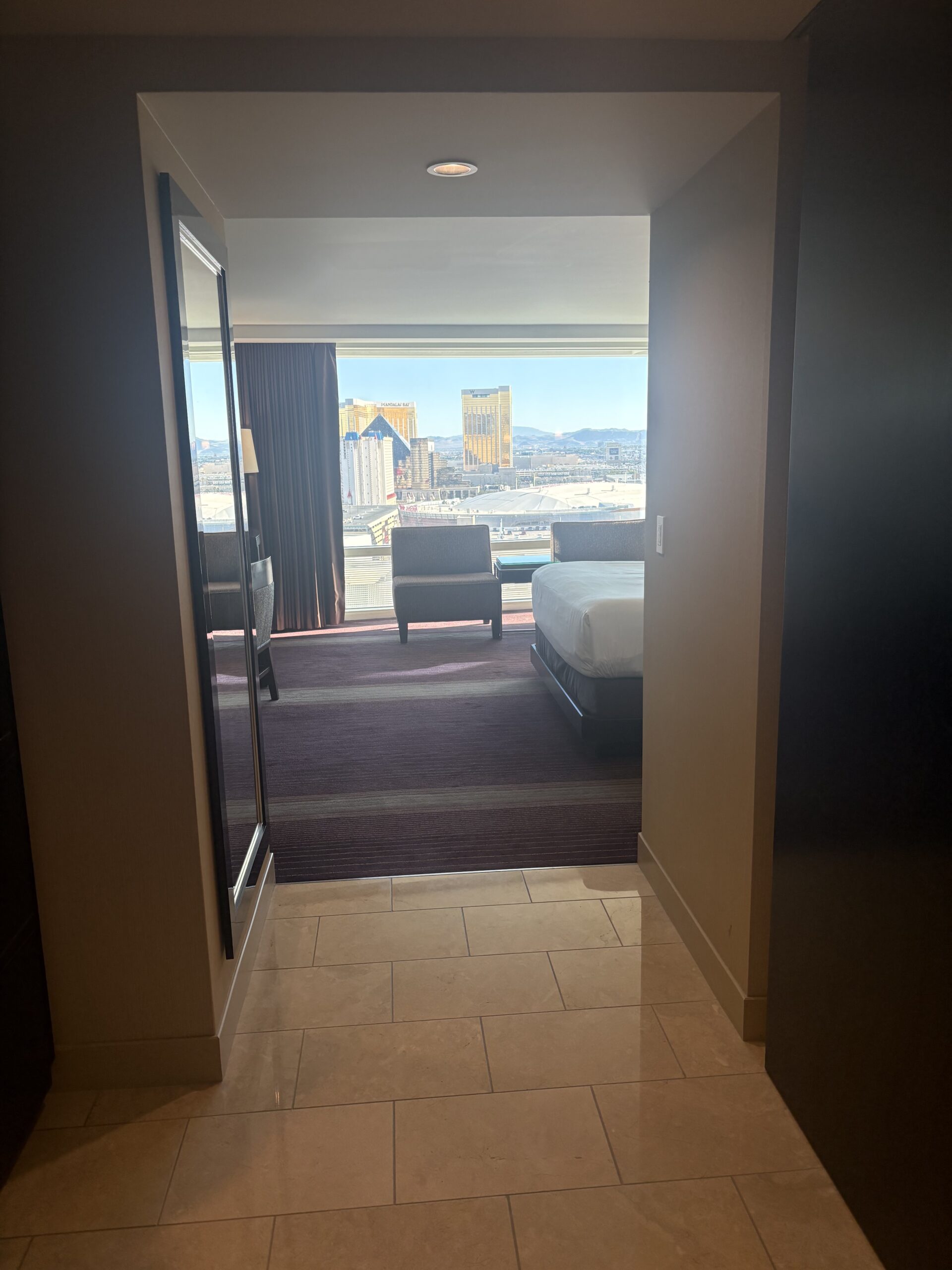 View down the entry hall of an Aria room toward the corner window and bed
