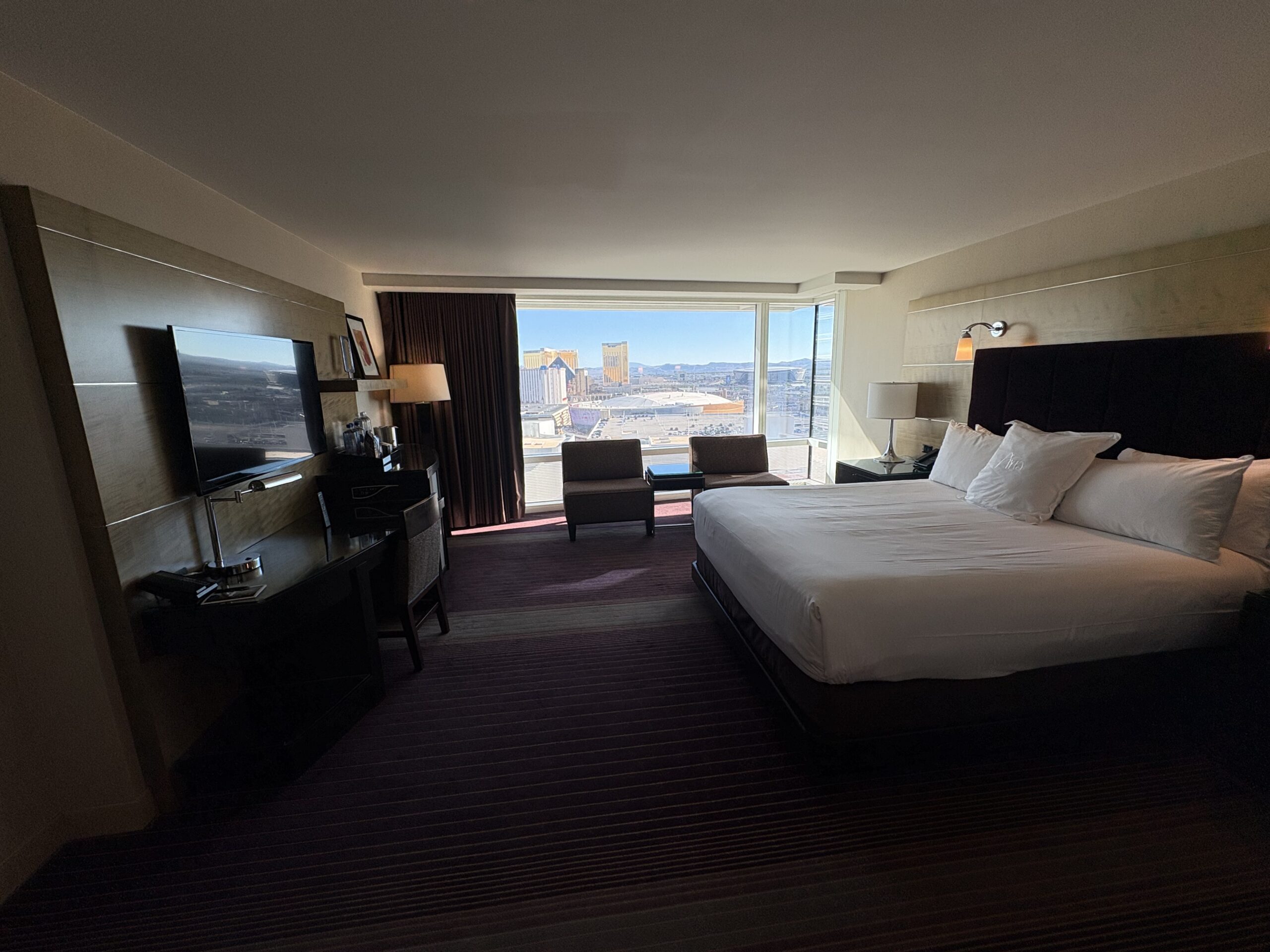 Aria king room with desk, TV, lounge chairs, and floor-to-ceiling corner window
