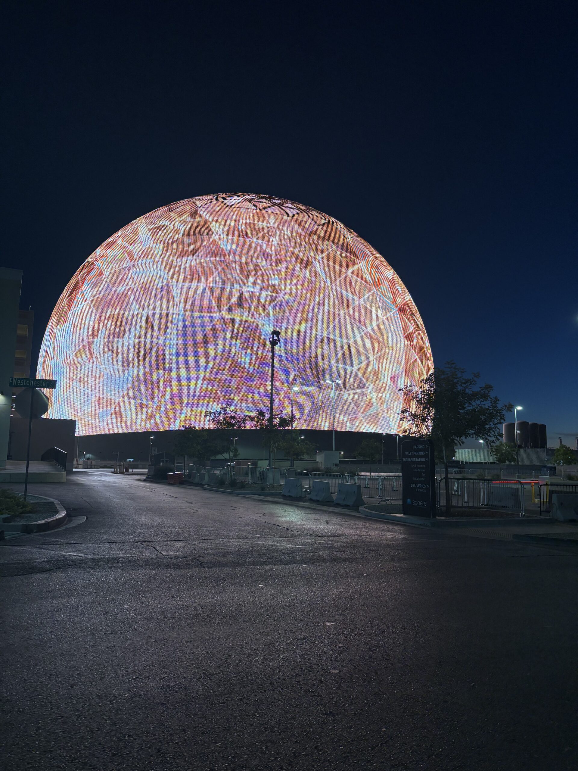 Las Vegas Sphere lit up at dawn, seen from Westchester Drive with signs for parking, valet and rideshare